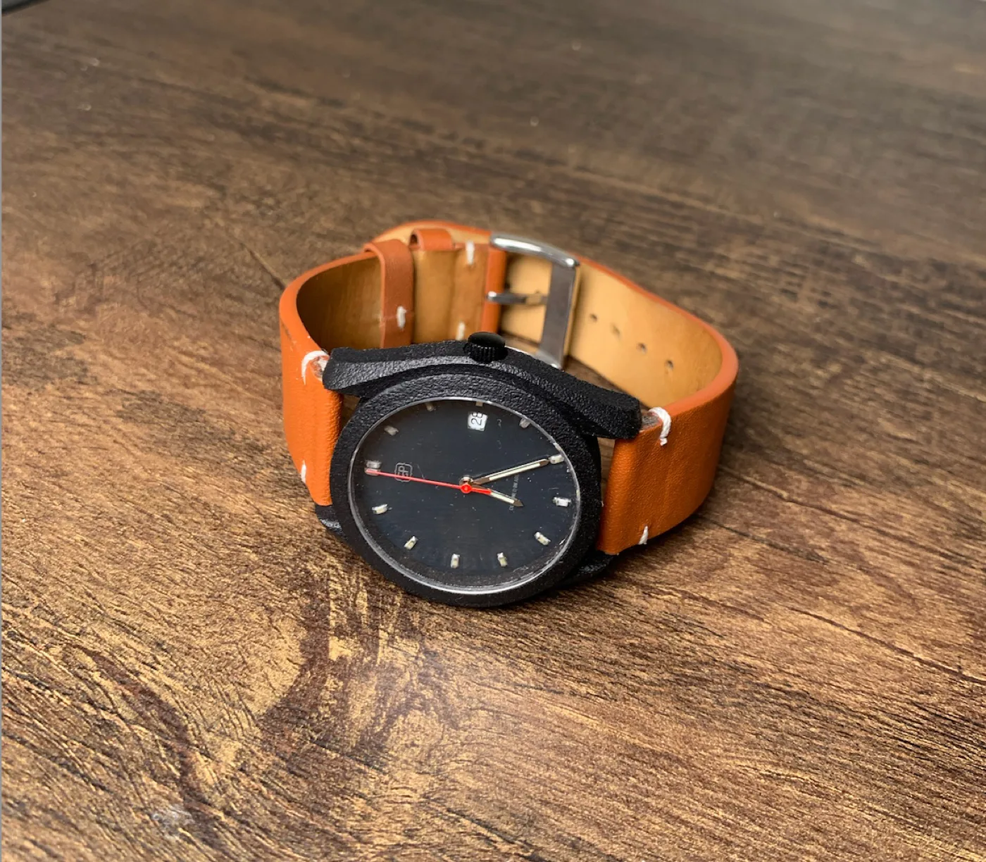 Completed black GP MK-1 watch with an orange leather band on a wooden workbench